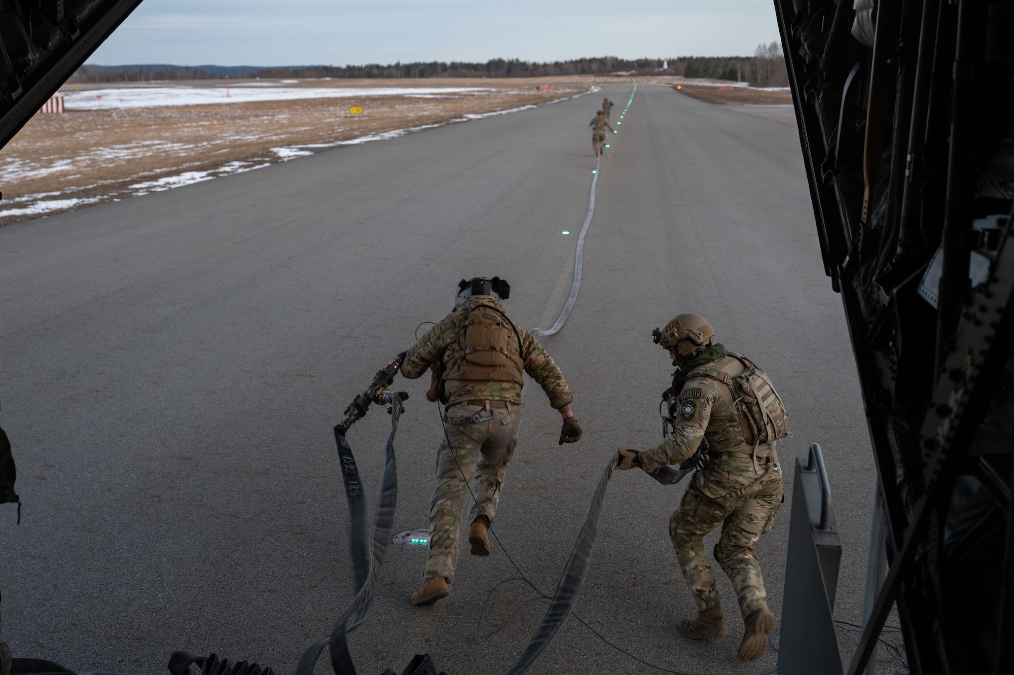 U.S. Air Force Forward Area Refueling Point (FARP) specialists assigned to the 100th Air Refueling Wing, sprint down the runway carrying fuel hoses, Norway, March 10, 2023.