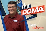 A smiling man wearing glasses has on a red shirt with the DCMA logo