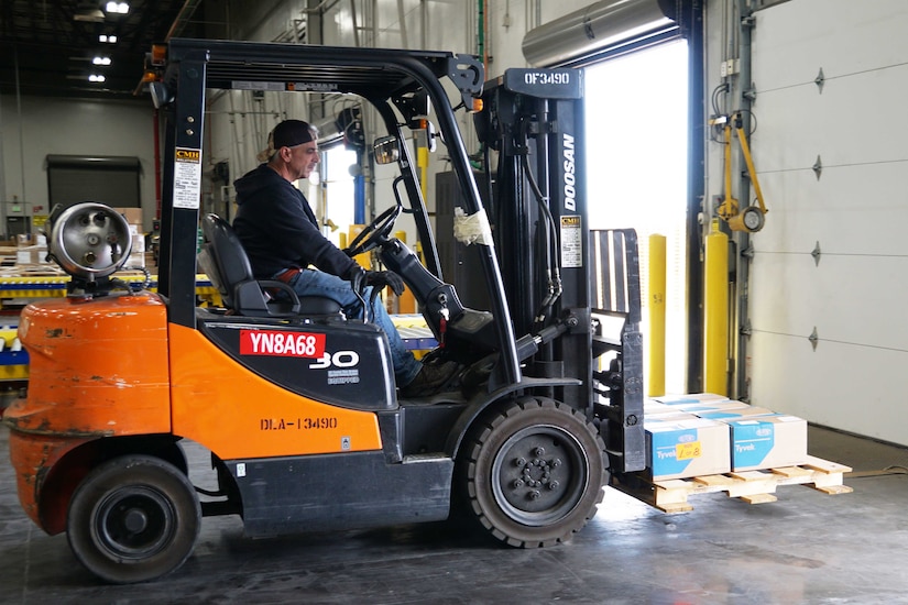 A man operates a forklift with a pallet containing supplies.