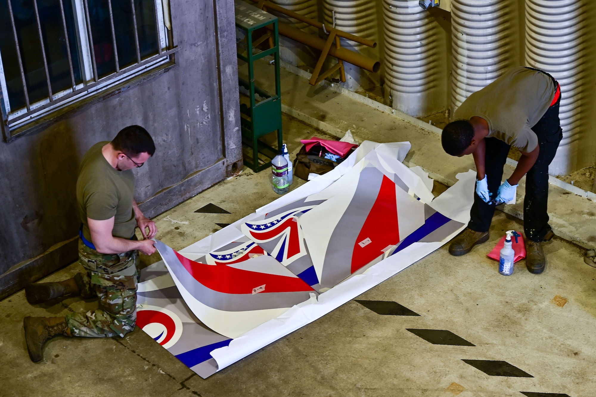 Staff Sgt. Matthew Campbell, 8th Maintenance Squadron aircraft structural maintainer craftsman, and Senior Airman Connor Young, 8th MXS aircraft structural maintenance journeyman, prepare a 70th anniversary heritage tail flash decal at Osan Air Base, Republic of Korea, May 1, 2023. The decals will be applied to U.S. Air Force and ROK Air Force assets to celebrate the two nation’s 70-year strong Alliance. (U.S. Air Force photo by Tech. Sgt. Timothy Dischinat)