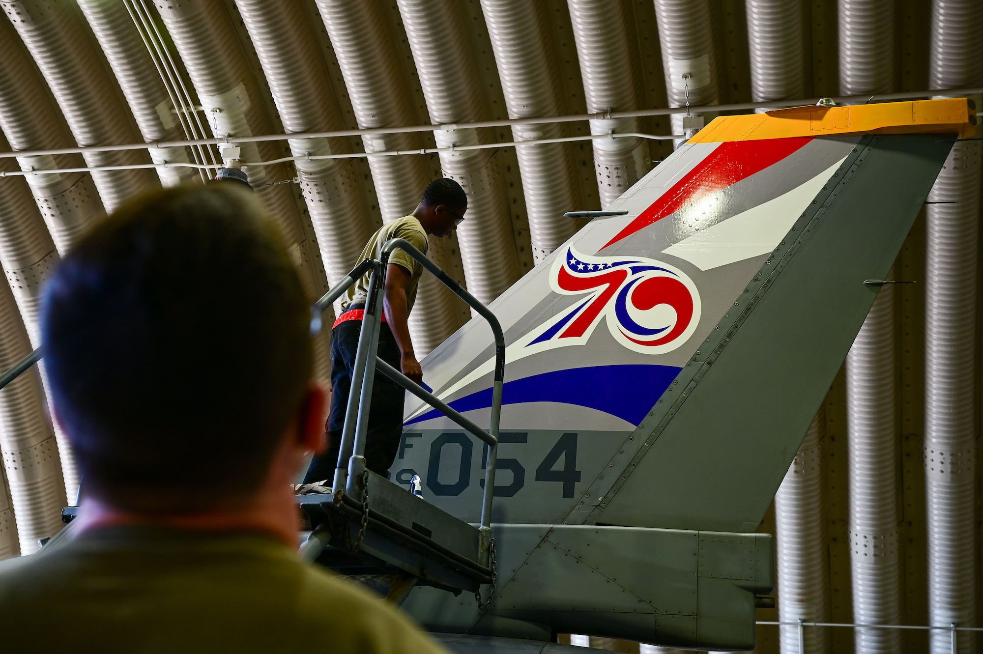 Staff Sgt. Matthew Campbell, 8th Maintenance Squadron aircraft structural maintenance (AMS) craftsman (left) assesses the application of a 70th anniversary heritage tail flash decal as Senior Airman Connor Young, 8th MXS AMS journeyman, looks on at Osan Air Base, Republic of Korea, May 1, 2023. Between measuring, application and preservation, the process can take up to 48 hours for each aircraft. (U.S. Air Force photo by Tech. Sgt. Timothy Dischinat)