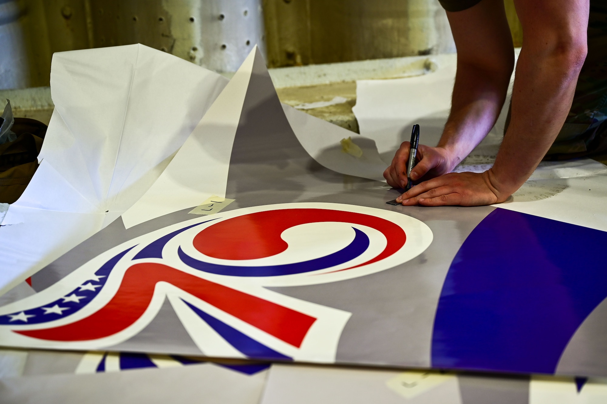 Staff Sgt. Matthew Campbell, 8th Maintenance Squadron aircraft structural maintenance craftsman, measures and marks a 70th anniversary heritage tail flash decal at Osan Air Base, Republic of Korea, May 1, 2023. Each piece of the decal must be measured, marked and cut to properly fit the tail of the F-16 Fighting Falcon. (U.S. Air Force photo by Tech. Sgt. Timothy Dischinat)