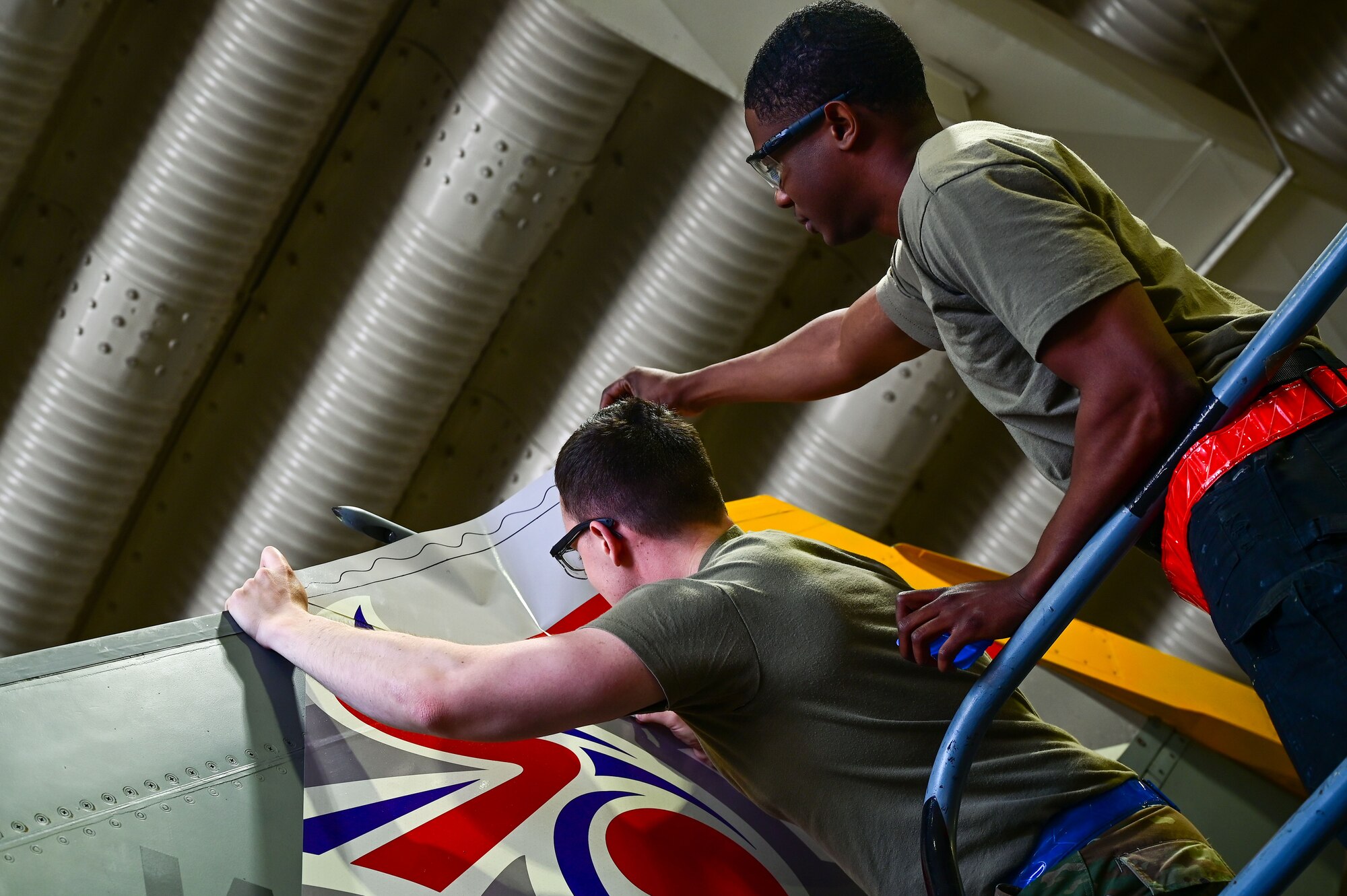Staff Sgt. Matthew Campbell, 8th Maintenance Squadron aircraft structural maintenance (AMS) craftsman, and Senior Airman Connor Young, 8th MXS AMS journeyman, apply a 70th anniversary heritage tail flash at Osan Air Base, Republic of Korea, May 1, 2023. 8th Fighter Wing and ROK Air Force 38th Fighter Group F-16s will bear the decals to symbolize the nations’ partnership during aerial missions. (U.S. Air Force photo by Tech. Sgt. Timothy Dischinat)