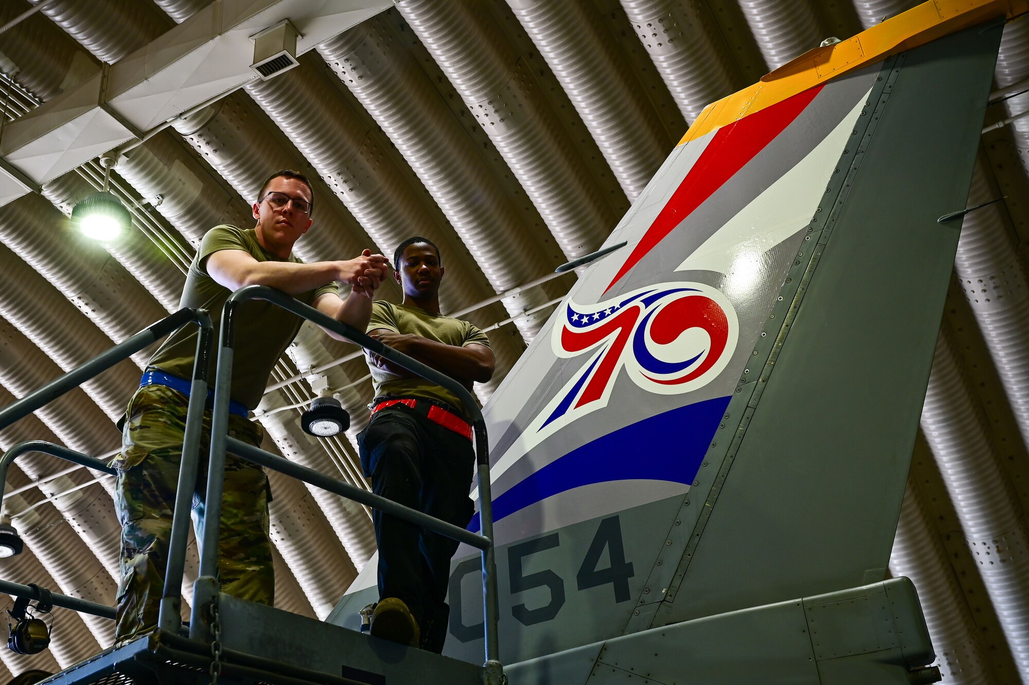 Staff Sgt. Matthew Campbell, 8th Maintenance Squadron aircraft structural maintenance (AMS) craftsman, and Senior Airman Connor Young, 8th MXS AMS journeyman, pose with the applied 70th anniversary heritage tail flash decal at Osan Air Base, Republic of Korea, May 1, 2023. After the decal is applied, sealed and dried for more than 24 hours, the aircraft is ready to fly. (U.S. Air Force photo by Tech. Sgt. Timothy Dischinat)