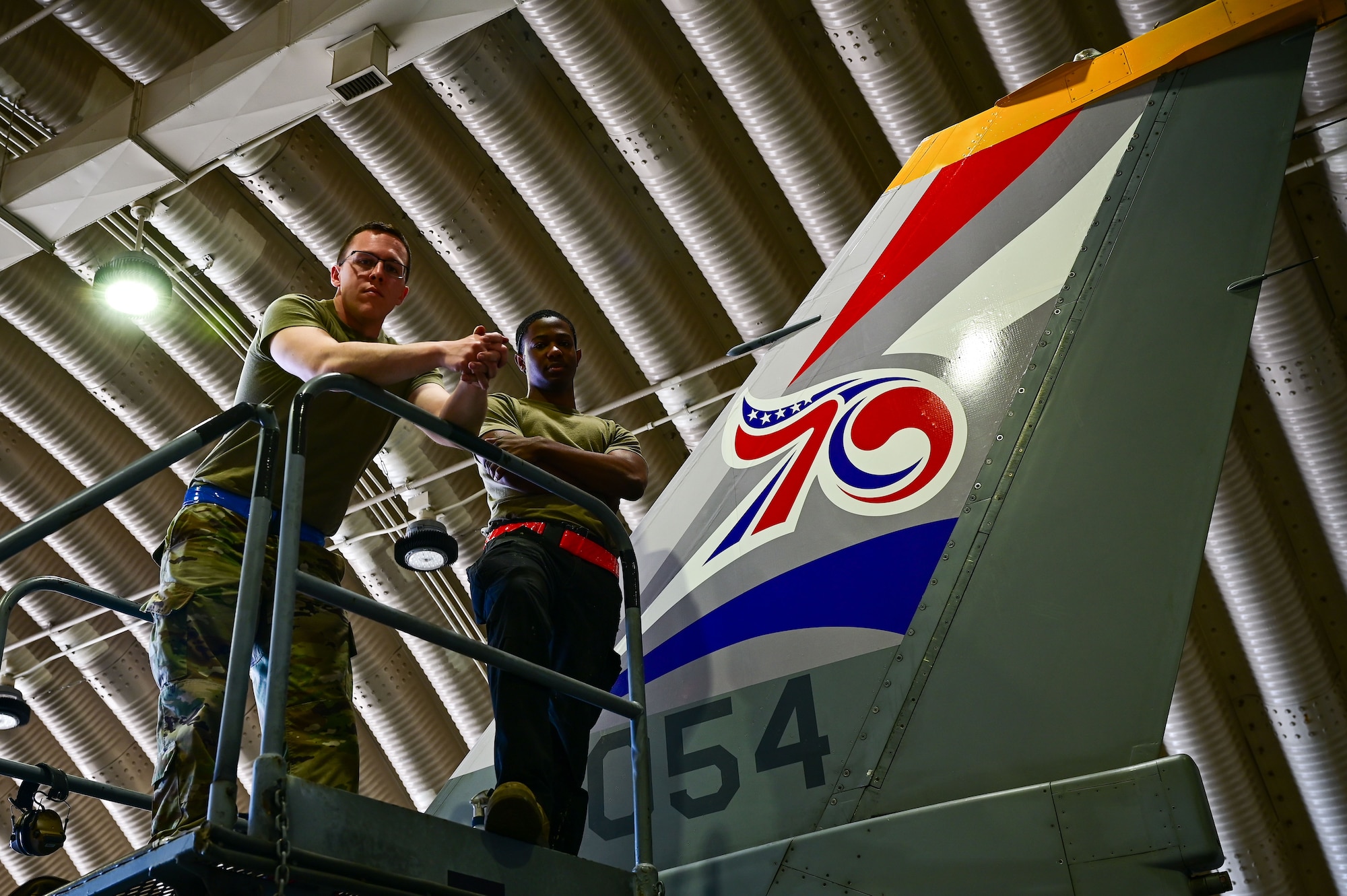 Staff Sgt. Matthew Campbell, 8th Maintenance Squadron aircraft structural maintenance (AMS) craftsman, and Senior Airman Connor Young, 8th MXS AMS journeyman, pose with the applied 70th anniversary heritage tail flash decal at Osan Air Base, Republic of Korea, May 1, 2023. After the decal is applied, sealed and dried for more than 24 hours, the aircraft is ready to fly. (U.S. Air Force photo by Tech. Sgt. Timothy Dischinat)