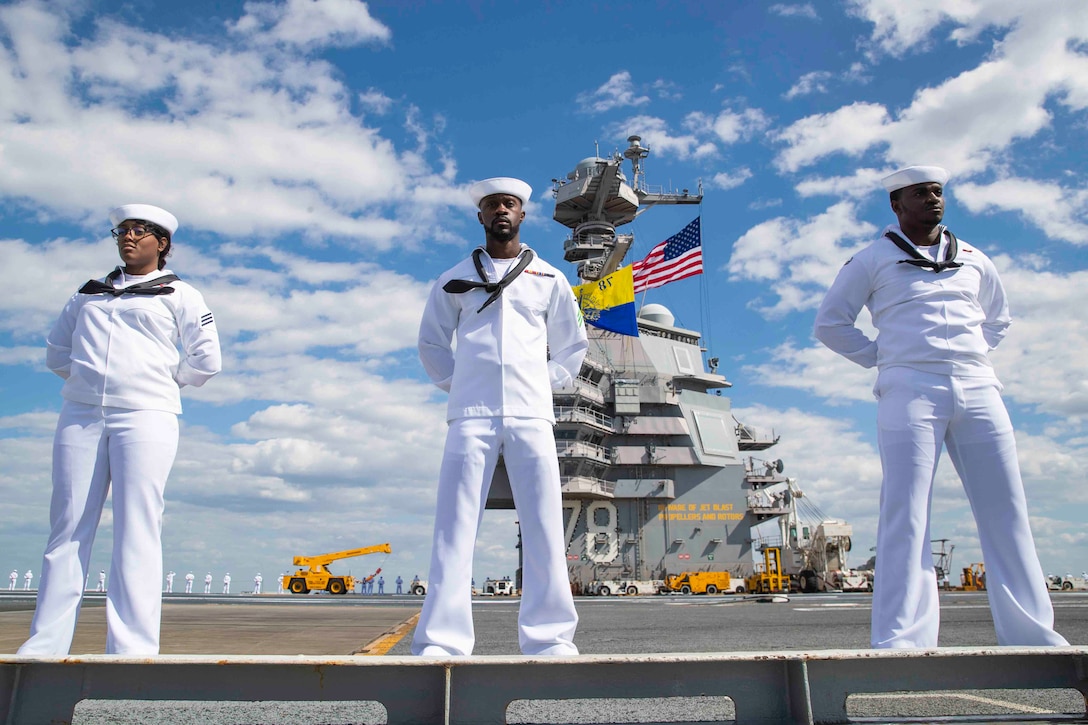 Three sailors stand on the deck of a ship.