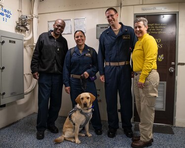 A dog sits in front of Sailors on a ship