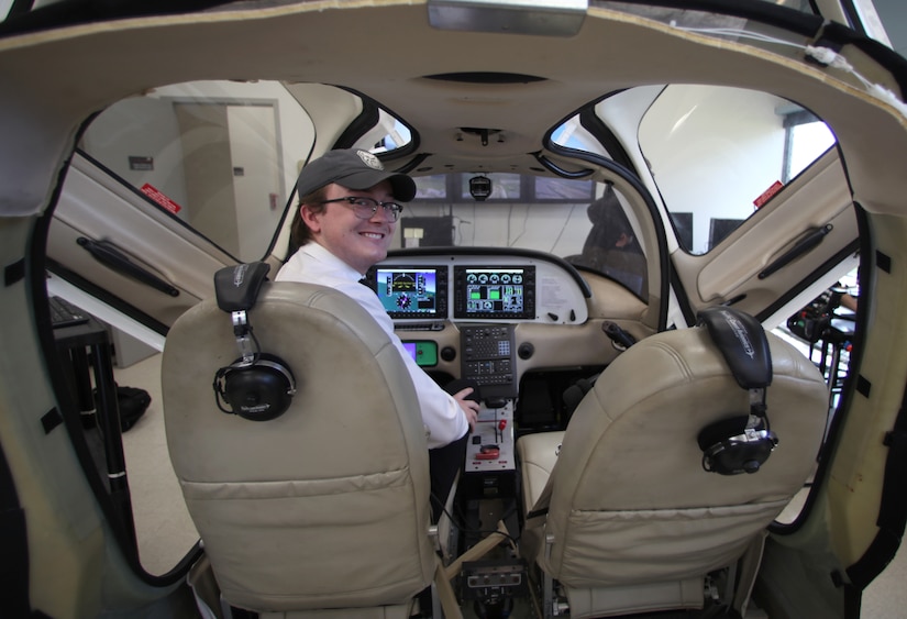 A student turns around and smiles while sitting in a mock cockpit.