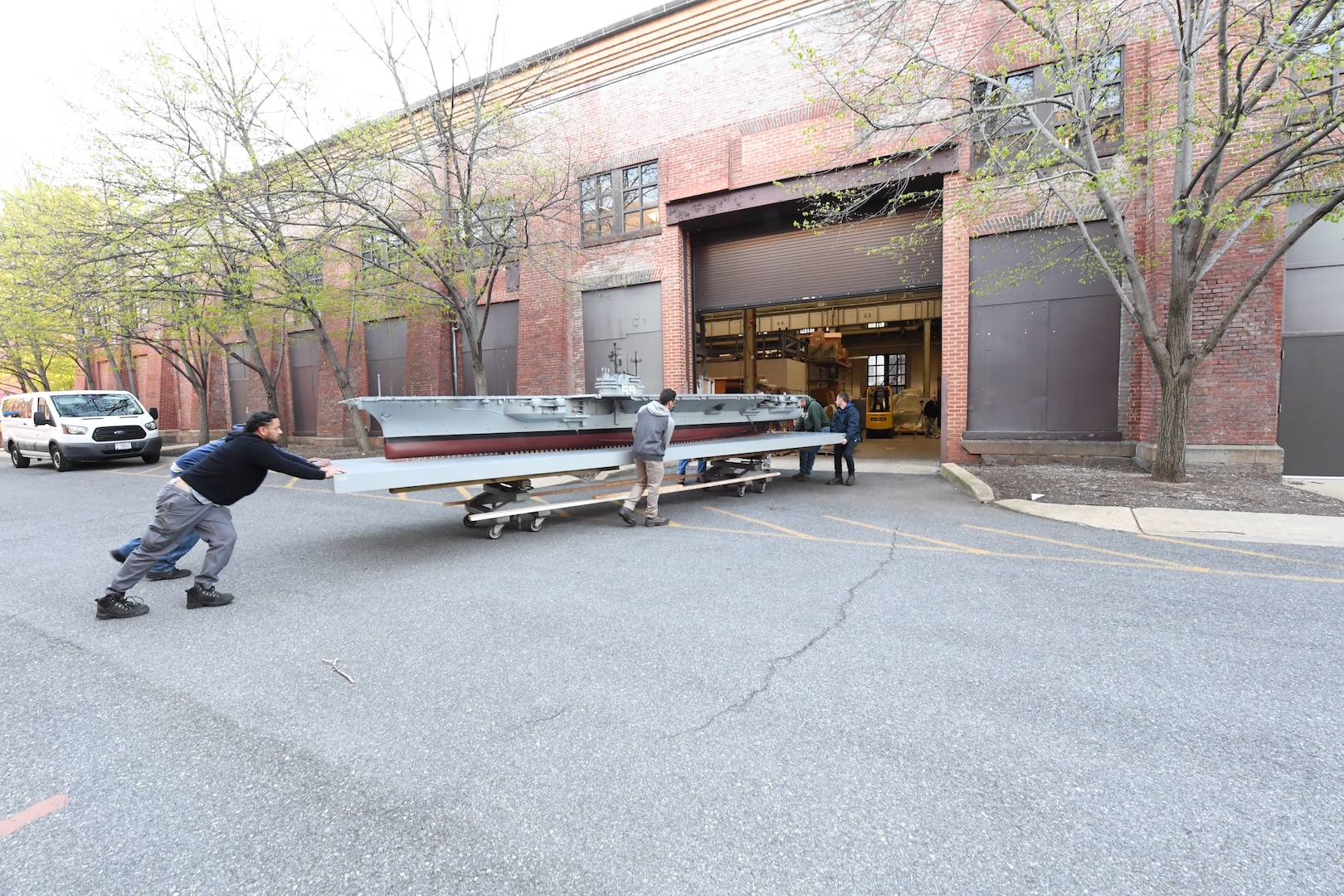 Carderock and museum staff carefully push the USS Forrestal model down an alley while dodging cars and potholes in order to get the model to a museum door large enough to accommodate the model during its transfer to its new home in the National Museum of the U.S. Navy at the Washington Navy Yard in Washington, D.C., on April 10. (U.S. Navy photo by Neubar Kamalian)