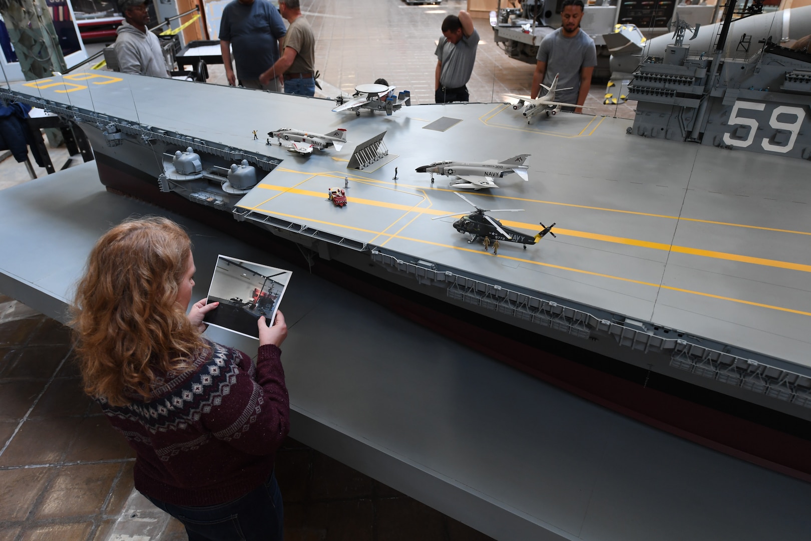 Naval Surface Warfare Center, Carderock Division’s Jennifer Marland, the Assistant Curator with the Office of the Curator, carefully examines a photograph to ensure all parts and pieces of the USS Forrestal model are put back correctly after the move to its new home in the National Museum of the U.S. Navy at the Washington Navy Yard in Washington, D.C., on April 10. (U.S. Navy photo by Neubar Kamalian)