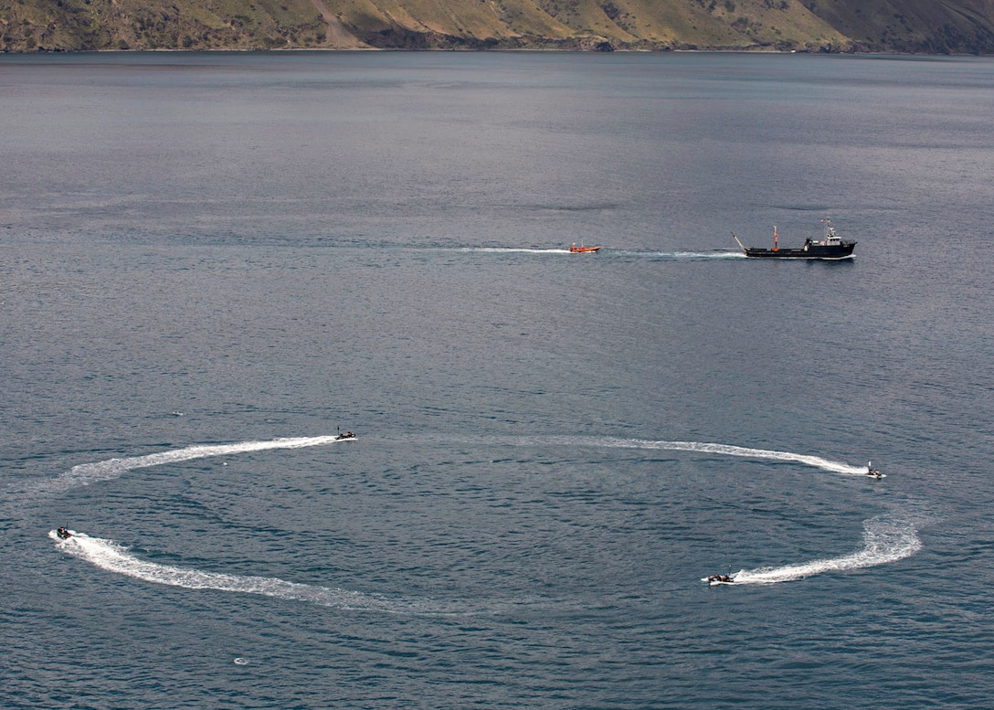 Four boats travel in a circle in a body of water as a larger boat passes by.