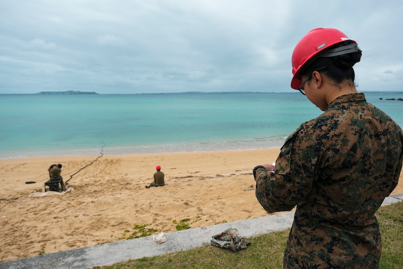 A Marine stands on the beach and looks down.