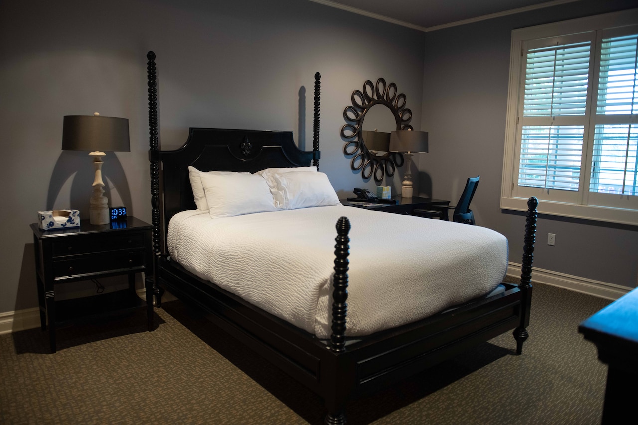 A large bed sits in the middle of a room beside a nightstand and a desk.