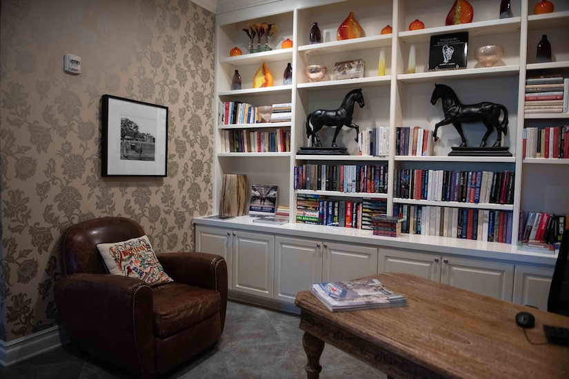 A chair and desk site beside a full-wall bookshelf filled with books and vases.