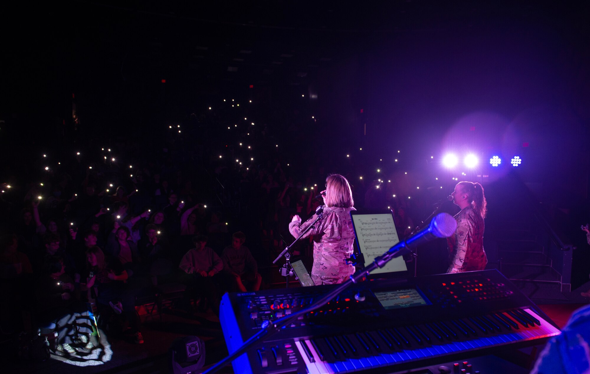 Lights from cell phones shine in seating area while band plays on stage in foreground