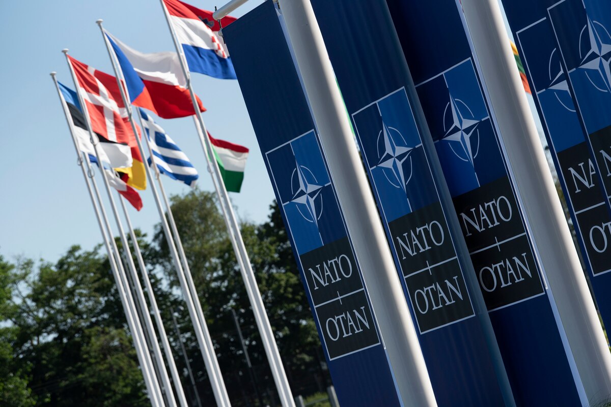 Banners which read "NATO OTAN" hang from poles near flags from multiple nations.