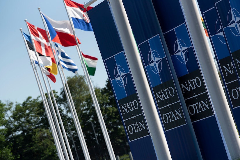 Banners which read "NATO OTAN" hang from poles near flags from multiple nations.
