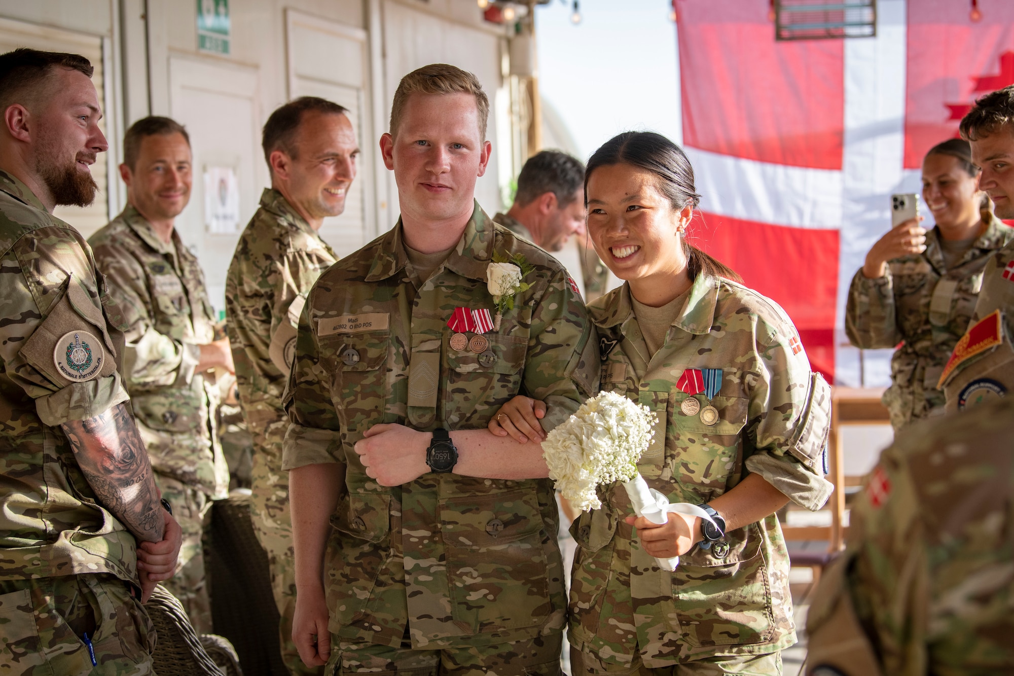 Sergeant 1st Class Mads Petersen, left, and Sergeant 1st Class Signe Li Jakobsen, right, Danish National Support Element quartermasters, walk down the aisle during their wedding at Ali Al Salem Air Base, Kuwait, May 3, 2023.