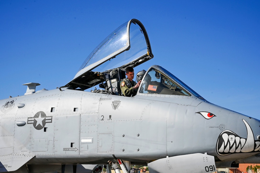 A pilot sits in the cockpit of a plane while checking his helmet.