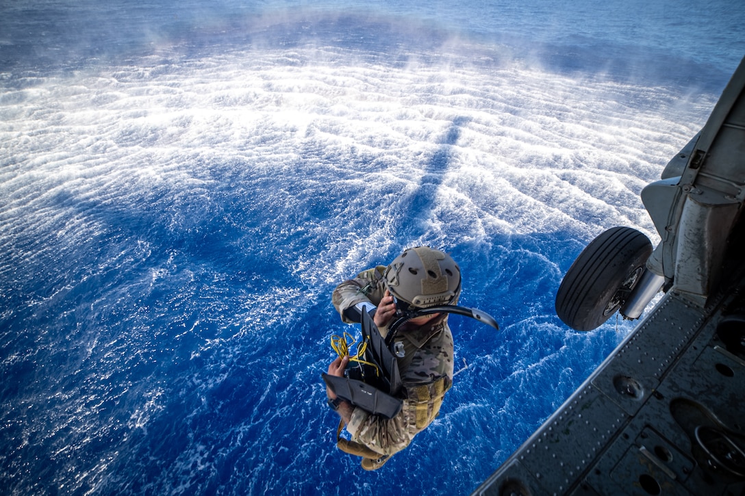 A sailor holding flippers jumps out of a helicopter into the ocean.