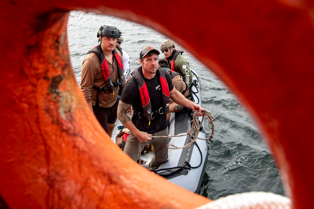A group of service members stand in a boat as seen through a porthole.