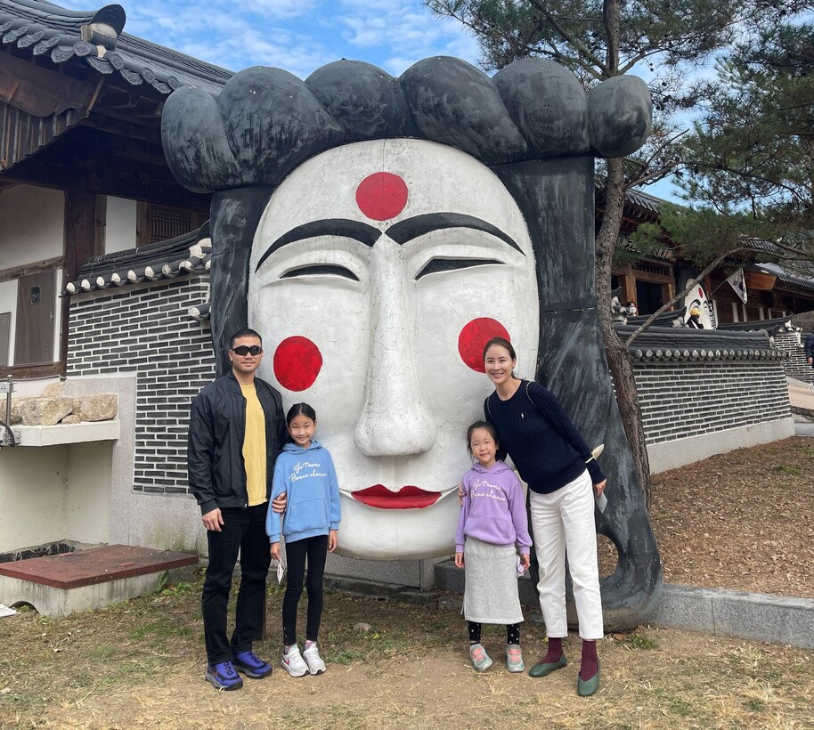 a family of four stand in front of a large Korean mask sculpture