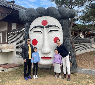 a family of four stand in front of a large Korean mask sculpture