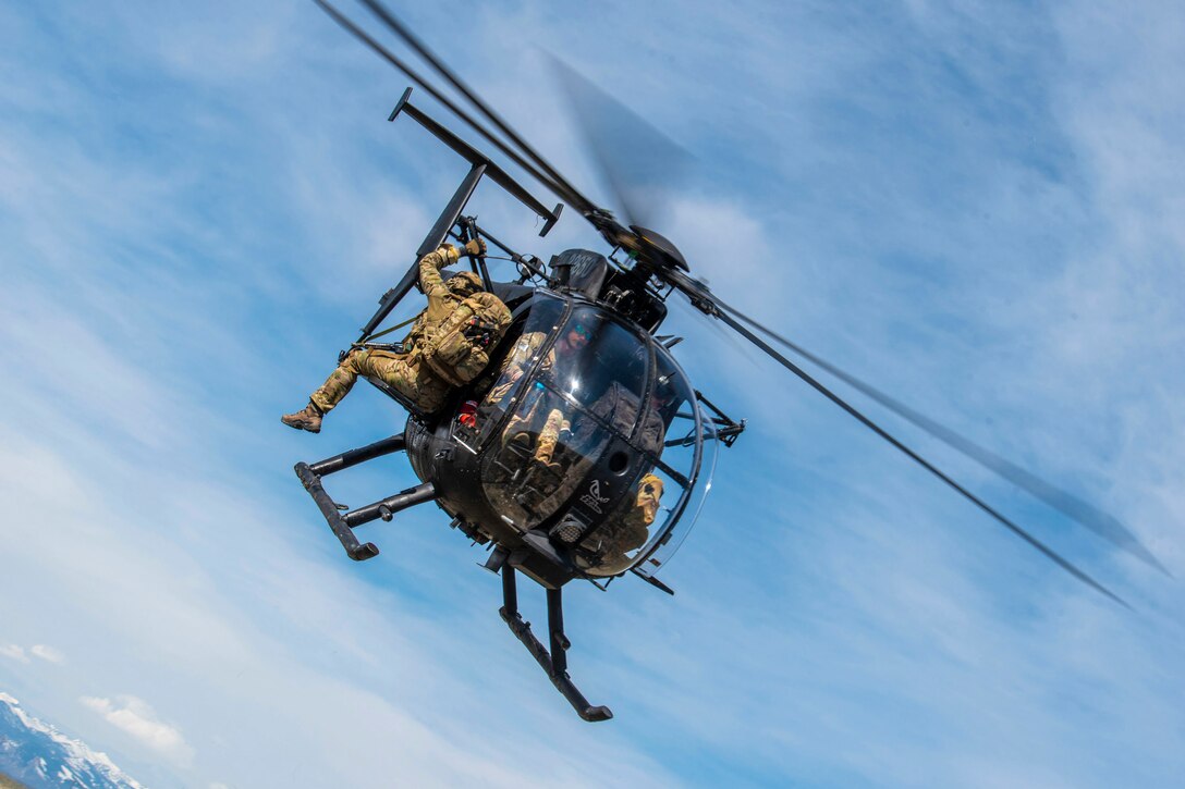 An airman hangs onto the side of an airborne helicopter.