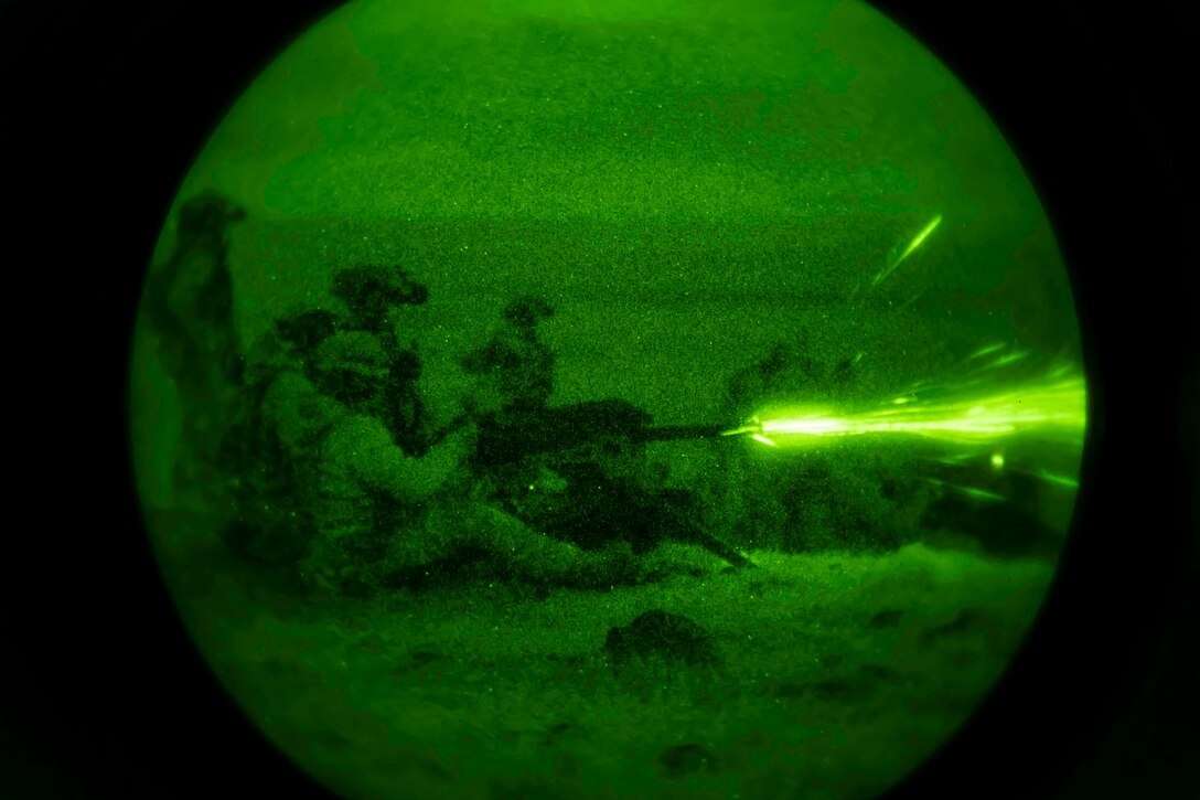 Airmen illuminated by green light fire a weapon.
