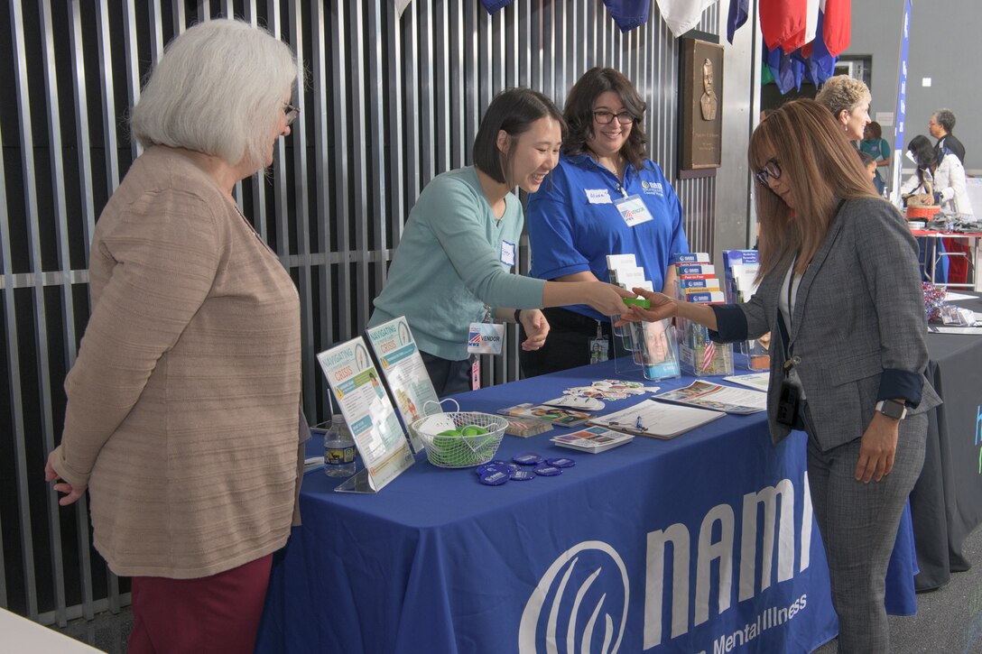 A table of volunteers hand out information during a Health and Safety expo for Defense Logistics Agency employees.