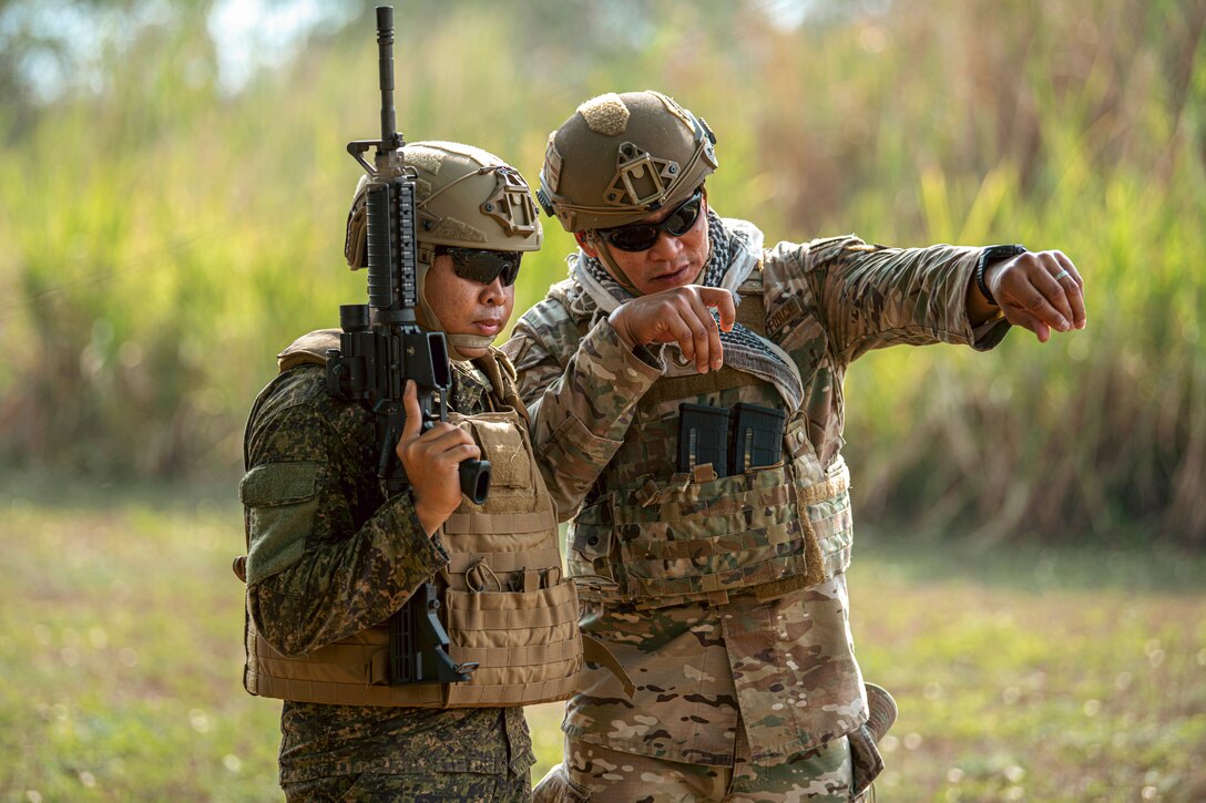 U.S. and Philippine airmen talk in a field near tall grass.