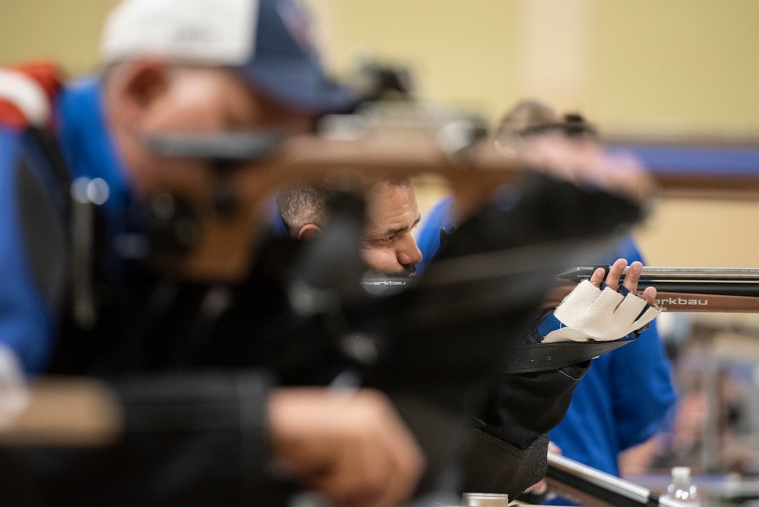 An RSM shooting his air rifle is framed by another competitors rifle and arm.