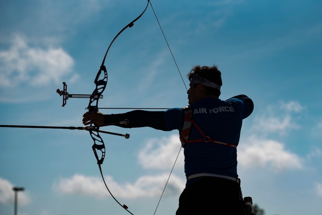 An archer is silhouetted against a partially cloudy blue sky.