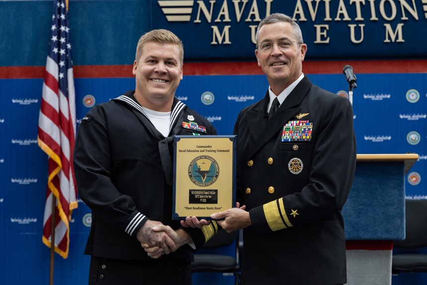 Rear Adm. Pete Garvin, right, commander, Naval Education and Training Command (NETC), awards a plaque to Navy Diver 1st Class Chase S. McCain, assigned to Naval Diving and Salvage Training Center Panama City, NETC’s fiscal year 2022 Sailor of the Year (SOY), during NETC’s SOY announcement and award ceremony at the National Naval Aviation Museum in Pensacola, Florida, May 11, 2023. NETC's mission is to recruit, train and deliver those who serve our nation, taking them from street-to-fleet by forging civilians into highly skilled, operational and combat ready warfighters. (United States Navy photo by Mass Communication Specialist 2nd Class Zachary Melvin)