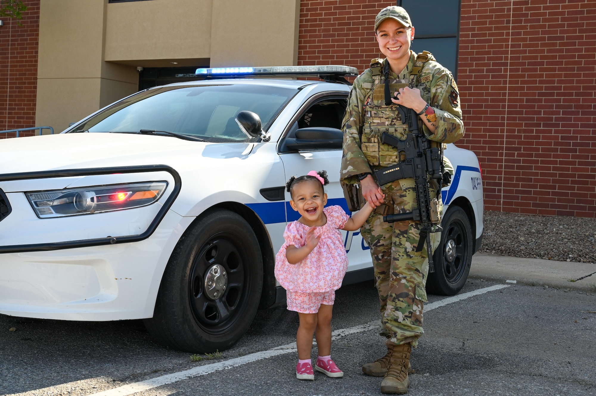 U.S. Air Force Senior Airman Maria Fox, 97th Security Forces Squadron patrolman, stands outside her patrol car with her daughter, Alina, at Altus Air Force Base, Oklahoma, May 9, 2023. There are 120,618 active duty Air Force service members with children. (U.S. Air Force photo by Senior Airman Kayla Christenson)