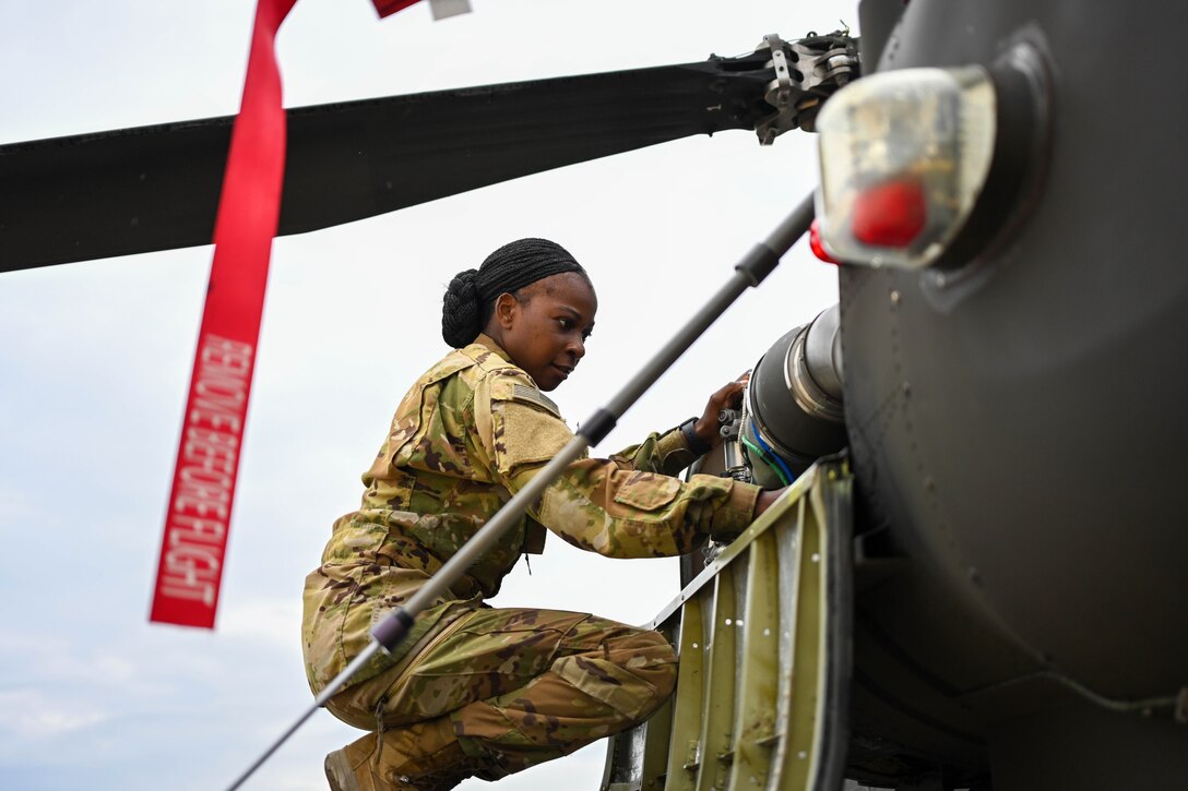 A soldier squats down while inspecting an Apache helicopter.