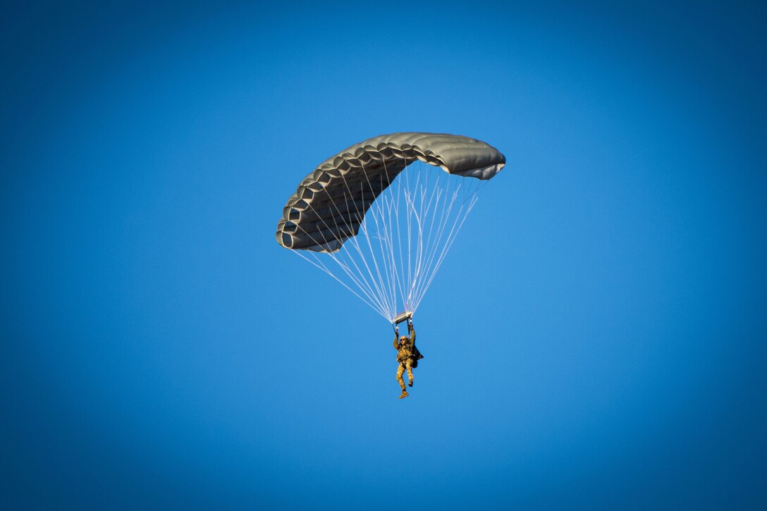 An airman parachutes against a blue sky.