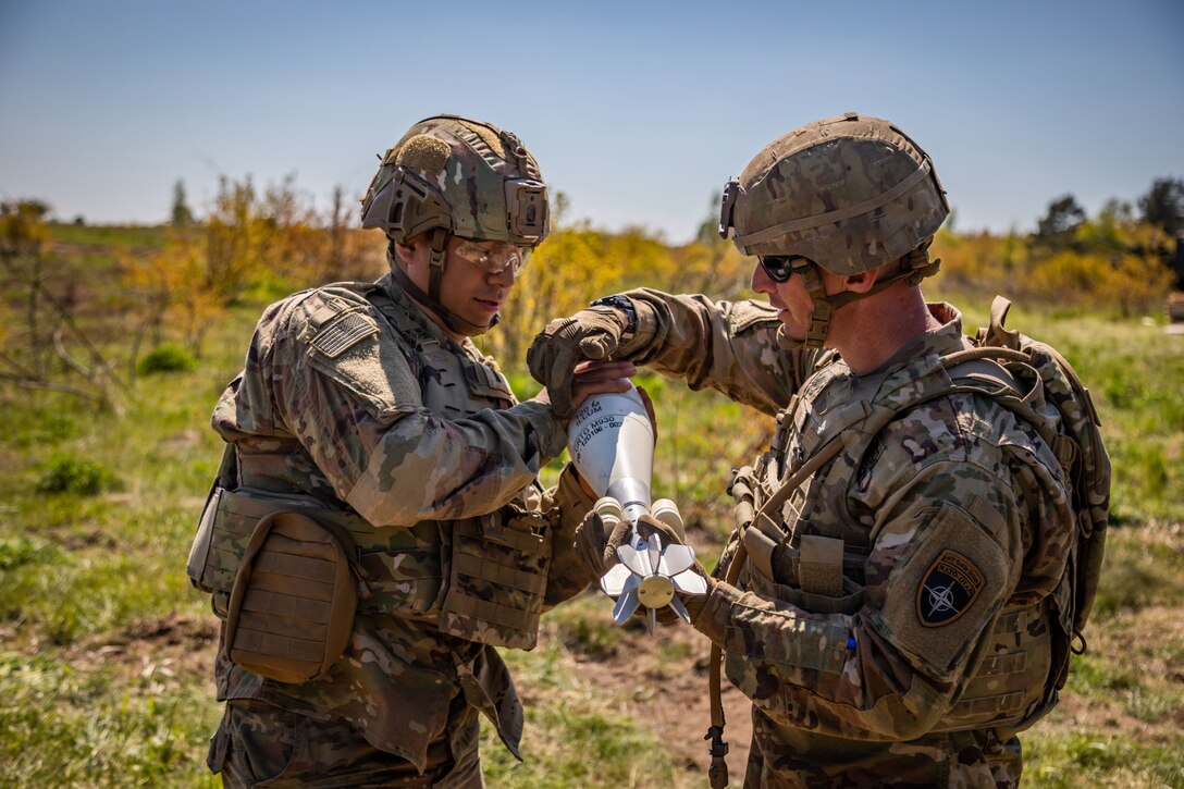 One soldier holds a mortar while another soldier prepares it for firing.