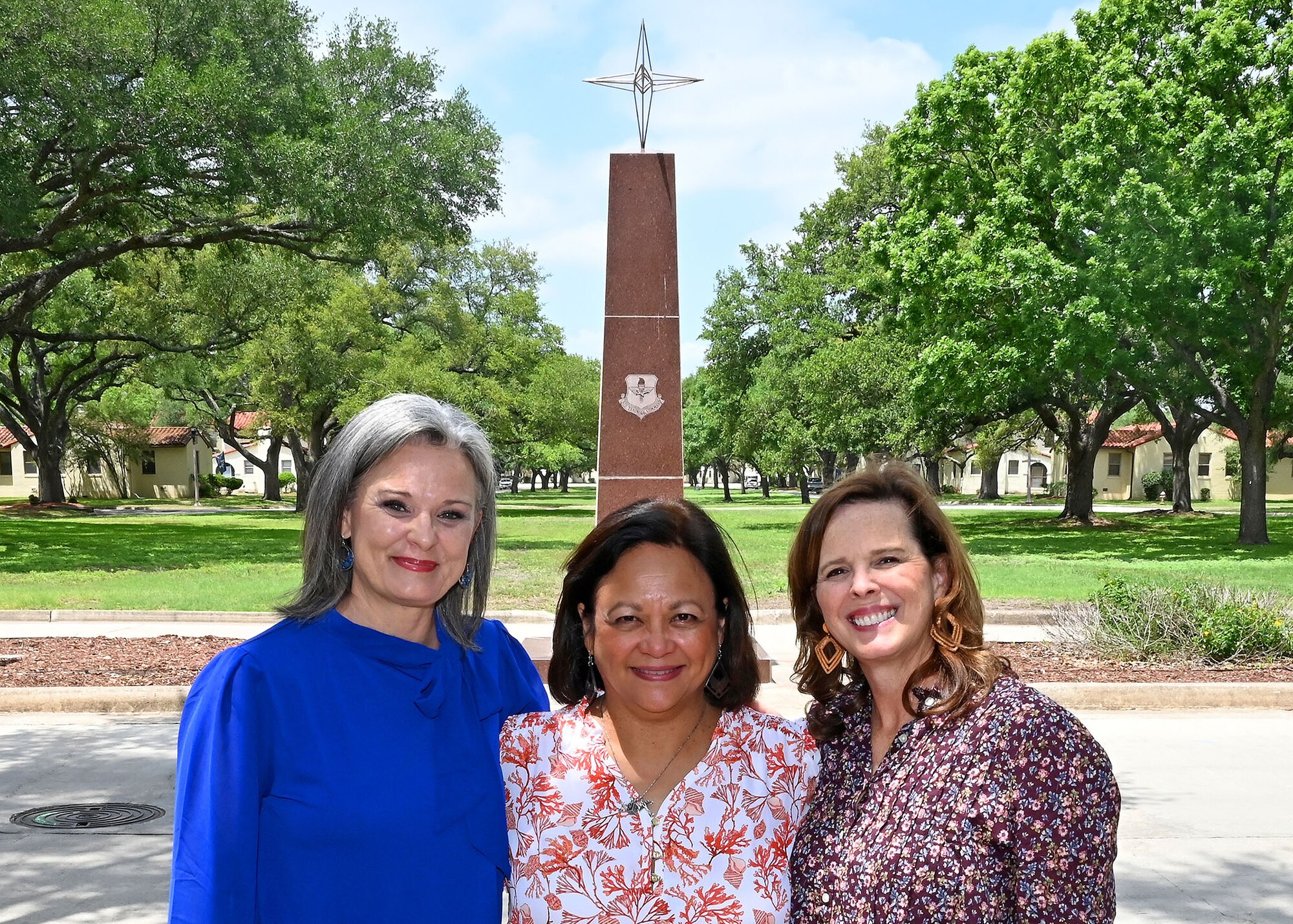 Three ladies stand in front of the Air Education And Training Command for a group photo.