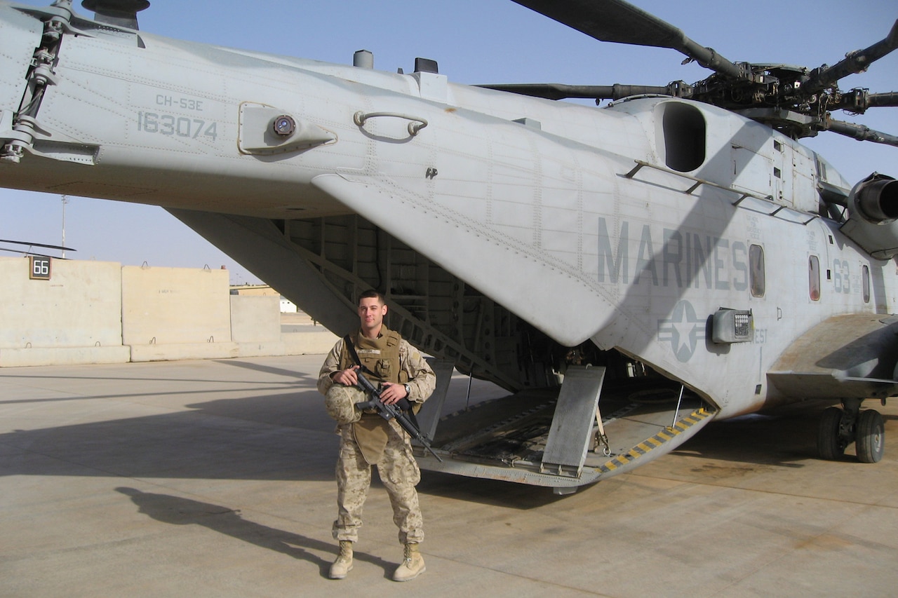 A Marine stands before a military aircraft.