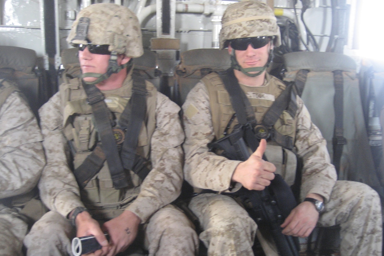 A Marine gives a thumbs up while seated and strapped into a military aircraft.