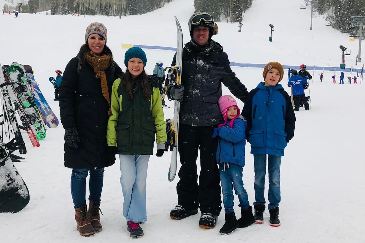 A family smiles while posing on a snowy ski slope.