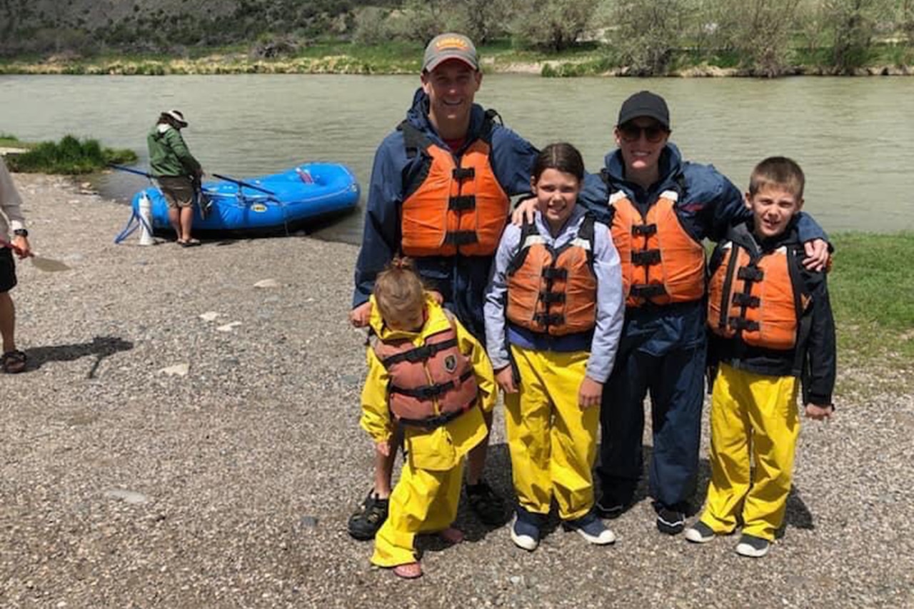 A family poses near a lake while wearing life jackets.