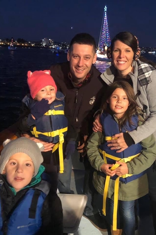 A family pose on a boat at night with holiday lights behind them.