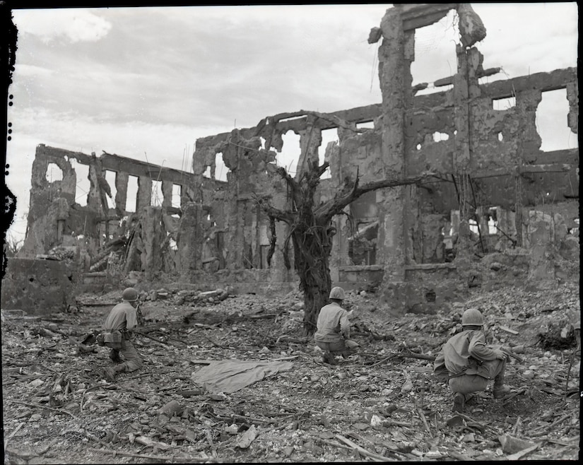Men hunker on their knees outside a destroyed building.