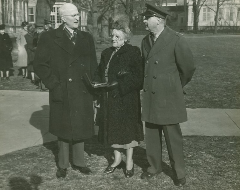 A woman holds a small box as two men stand on either side of her.