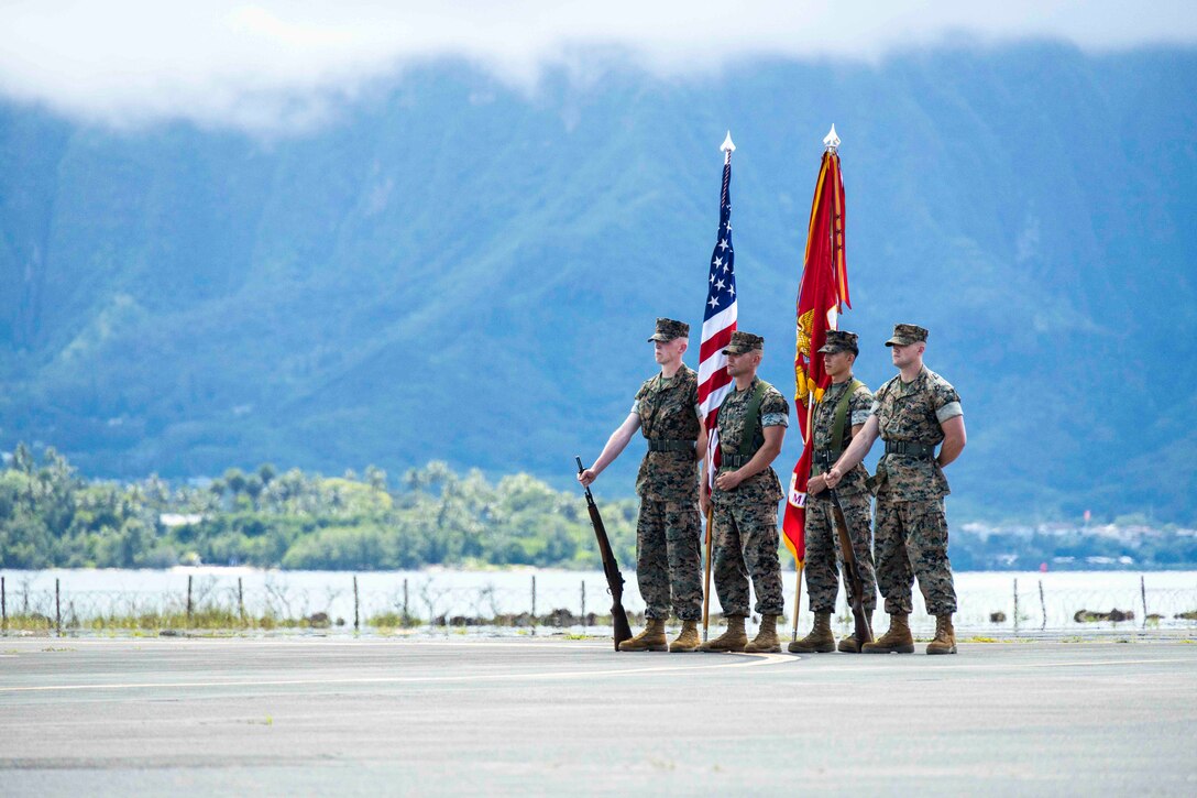 Four Marines stand in formation; some hold weapons while others hold flags.