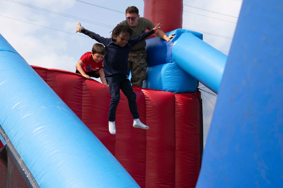 A child jumps into an inflatable obstacle as a service member and another child watch.