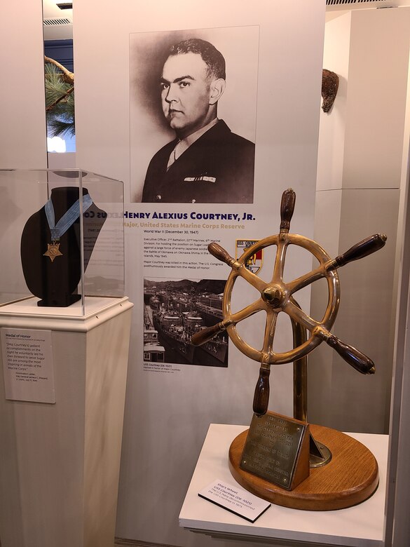 A display shows a Medal of Honor, a photo of a man and a wooden ship wheel.