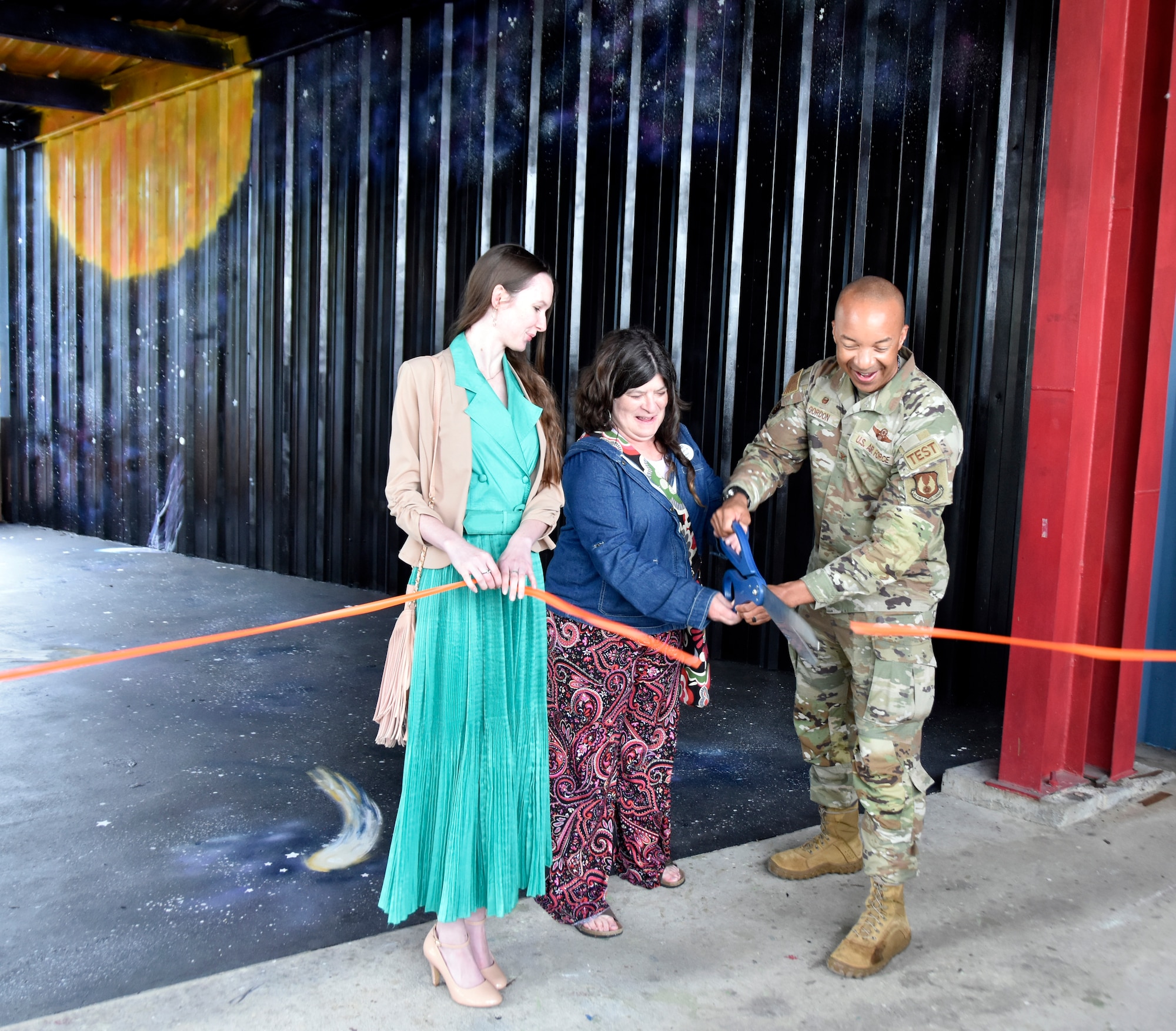 Arnold Engineering Development Complex Commander Col. Randel Gordon, joined by local artists Joy Snead, center, and Avery Wert, cuts the ribbon on the new space mural at the Hands-On Science Center in Tullahoma, Tenn., May 5, 2023. The mural depicting planets, stars and comets was made possible through a grant HOSC received from the Tennessee Arts Commission. With it, HOSC partnered with the Tullahoma Fine Arts Center, with which Snead and Wert are affiliated, to complete the mural. The ribbon cutting ceremony coincided with National Space Day. (U.S. Air Force photos by Bradley Hicks)